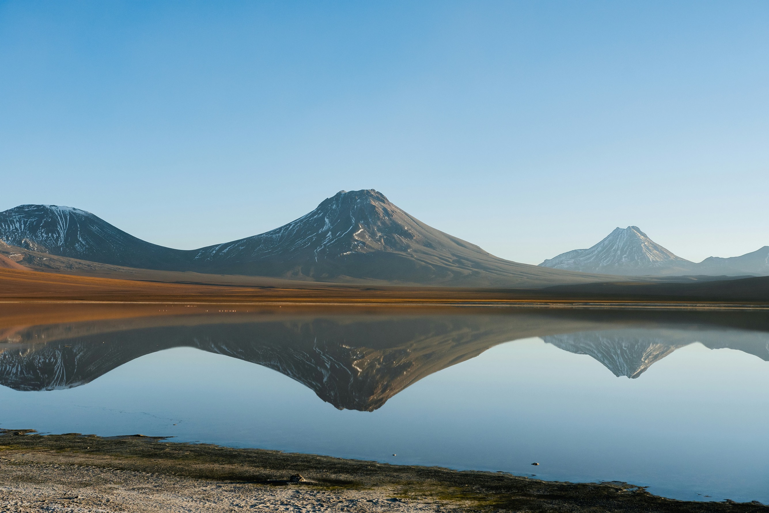 Snow-streaked mountains mirrored in a still lake at dawn